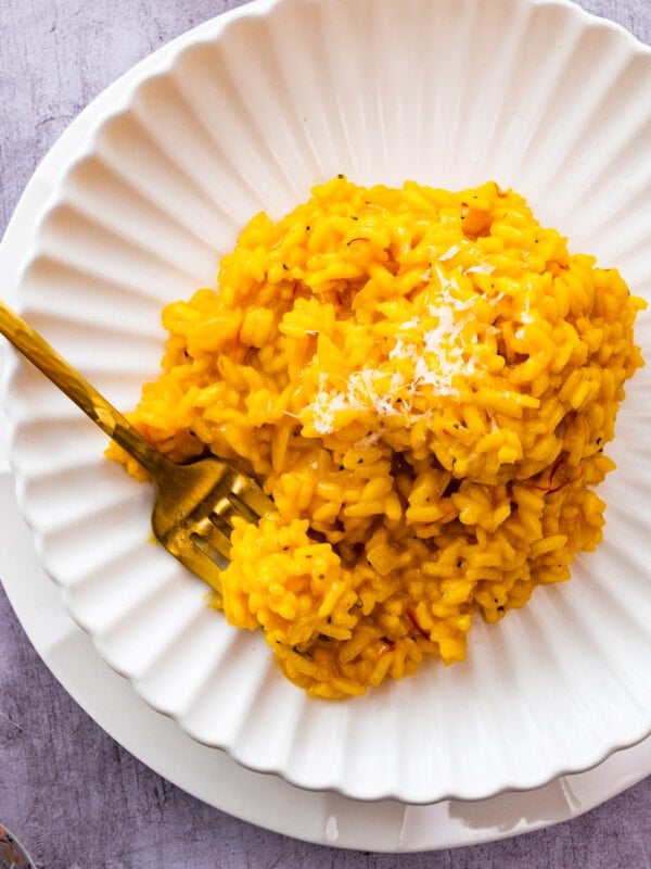 risotto all milanese on a white plate with parmigiano on top. close up with fork taking a bite.