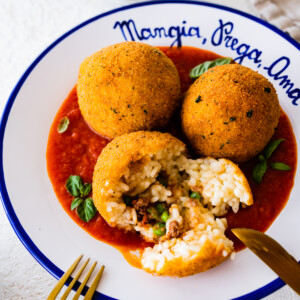 Sicilian arancini recipe on a blue and white plate with silverware.
