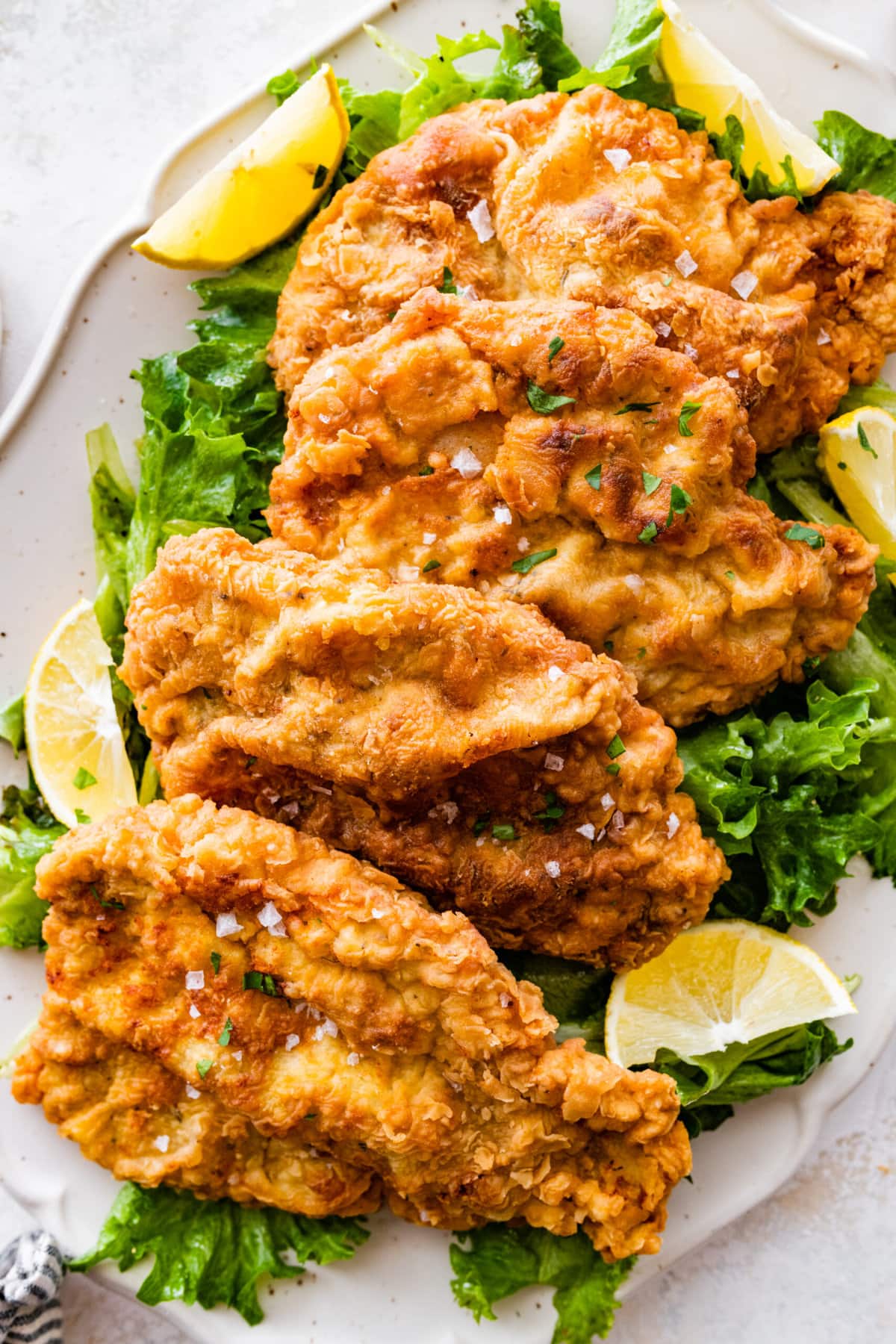 crispy fried pork chops on a plate with salad and lemon wedges. 