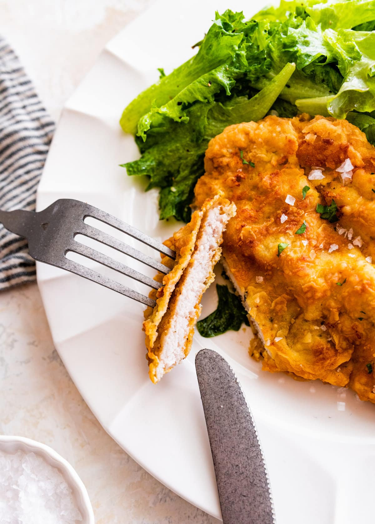 plated crispy pork chop with a bite taken out and side of salad.