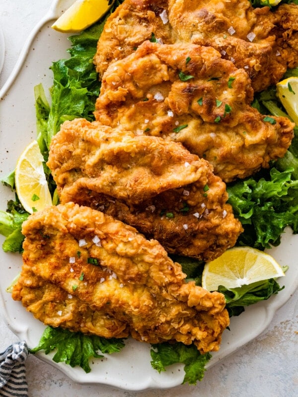 Crispy fried pork chops on a platter with lime wedges and greens.