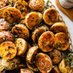 crispy potatoes on a serving platter with fresh herbs around it.