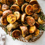 crispy potatoes on a serving platter with fresh herbs around it. Cover.