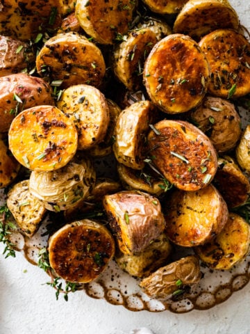 crispy potatoes on a serving platter with fresh herbs around it. Cover.