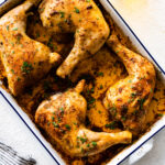 baked chicken leg quarters in a white baking dish. Fresh parsley on top as garnish.