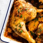 baked chicken leg quarters in a white baking dish. Fresh parsley on top as garnish. Close up.