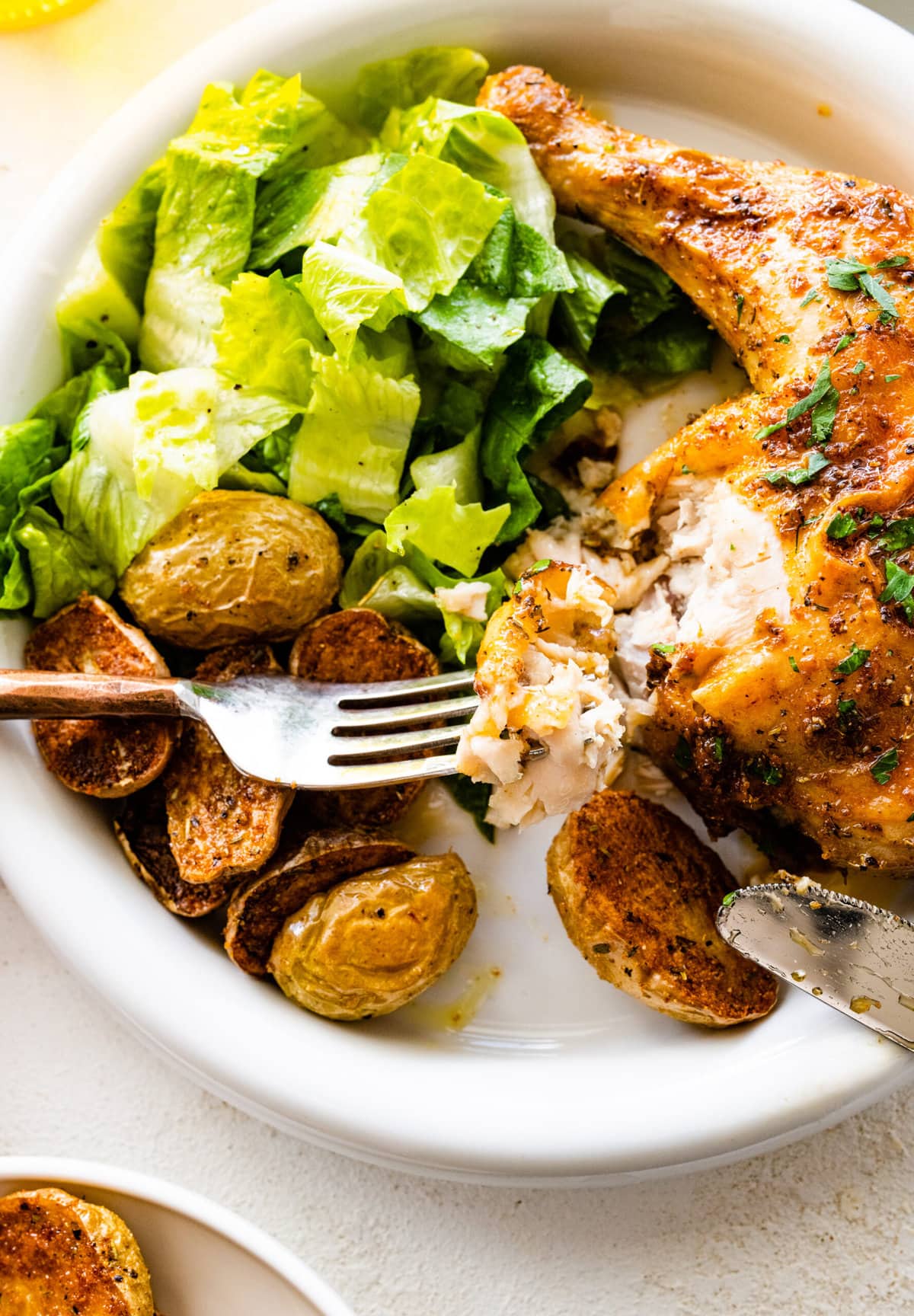platted baked chicken with potatoes and salad. Bite of chicken on a fork.