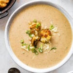 bowl of cauliflower soup with grilled bread on the side and whole pieces of roasted cauliflower on top.