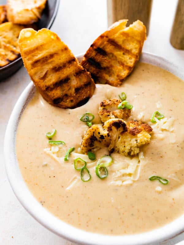 bowl of cauliflower soup with grilled bread on the side and whole pieces of roasted cauliflower on top.