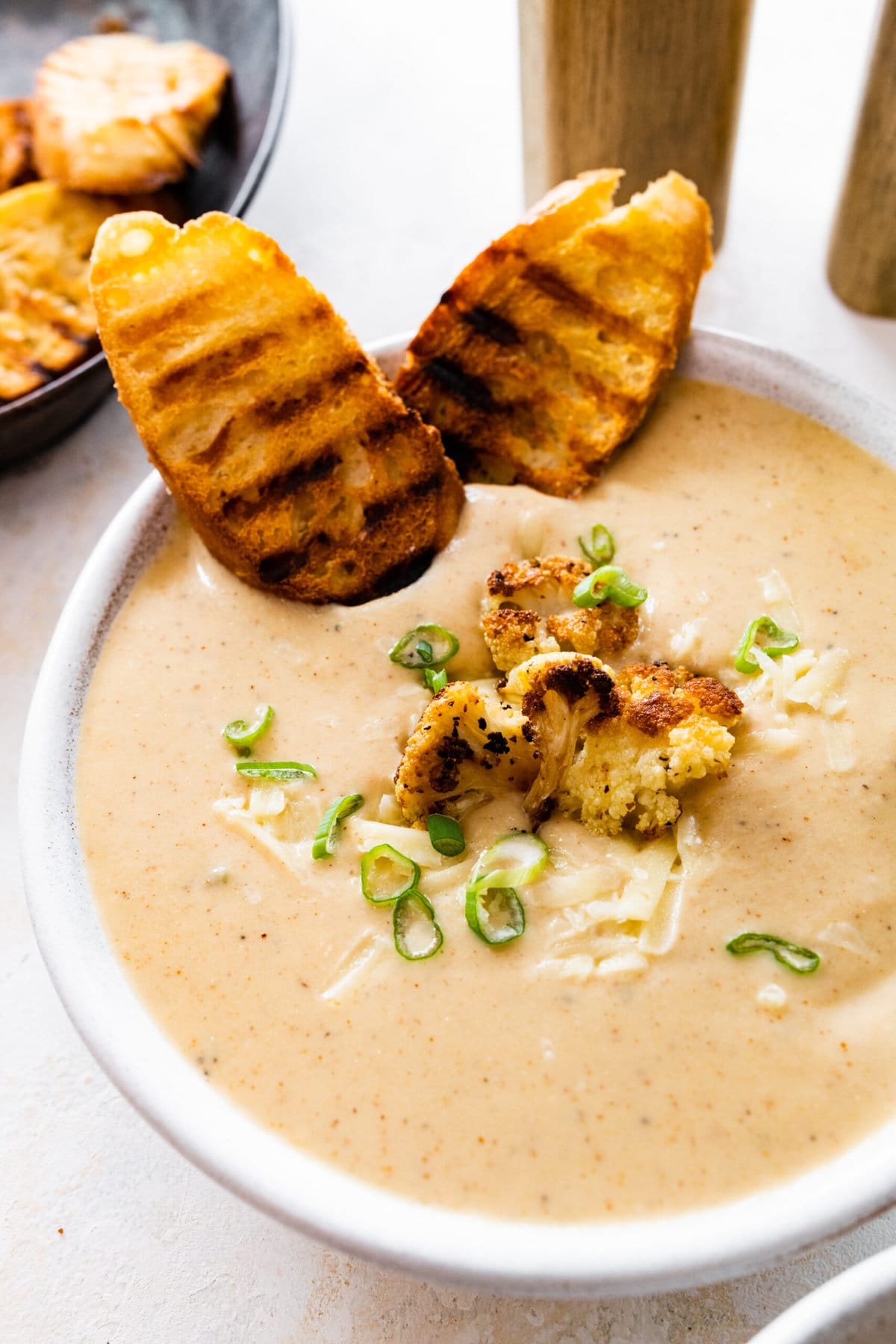 bowl of cauliflower soup with grilled bread on the side and whole pieces of roasted cauliflower on top.