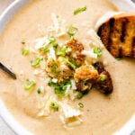 bowl of cauliflower soup with grilled bread on the side and whole pieces of roasted cauliflower on top.