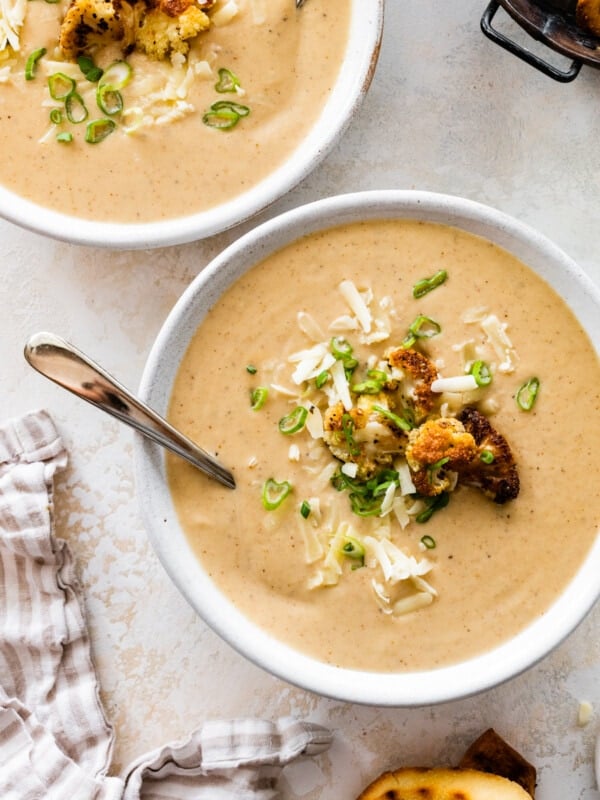 bowl of cauliflower soup with grilled bread on the side and whole pieces of roasted cauliflower on top.