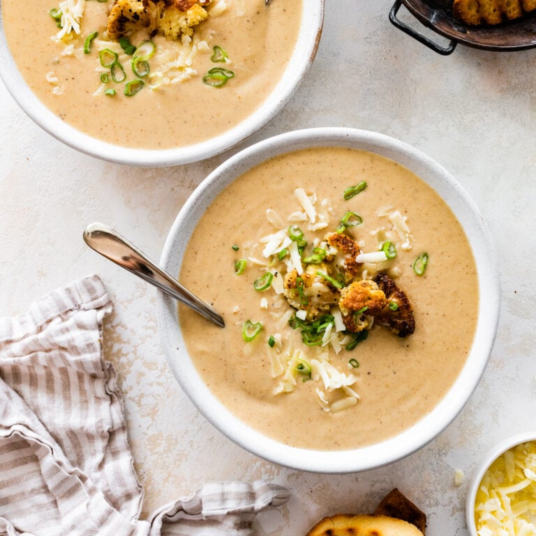bowl of cauliflower soup with grilled bread on the side and whole pieces of roasted cauliflower on top.