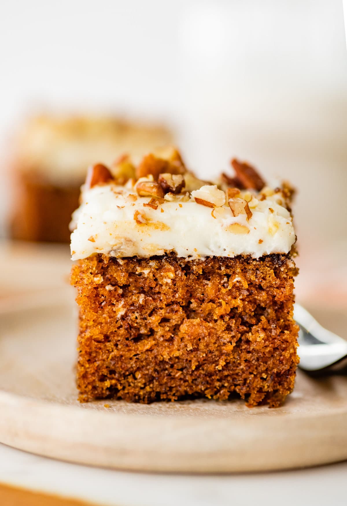a square slice of carrot cake with cream cheese frosting on a plate with a fork.