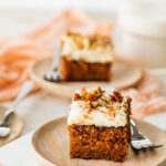 a square slice of carrot cake with cream cheese frosting on a plate with a fork.