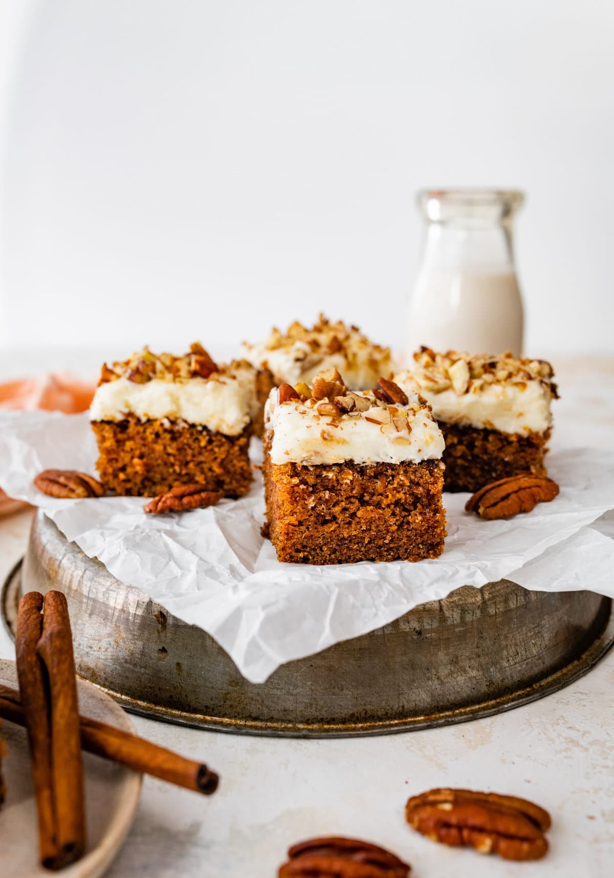 a tray of square slices of carrot cake with some pecans on the side.