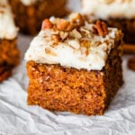 a square slice of carrot cake with cream cheese frosting on a plate.