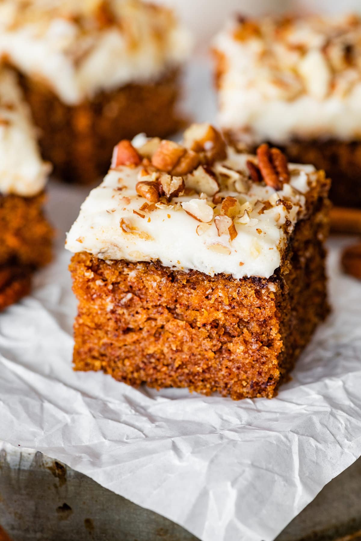 a square slice of carrot cake with cream cheese frosting on a plate.