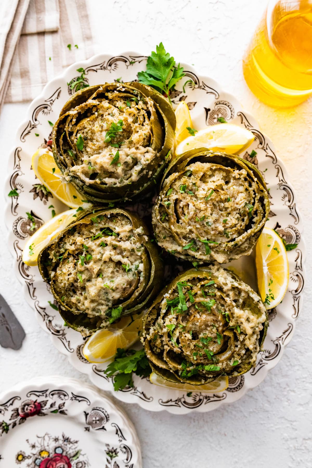 Cooked artichokes on a platter with lemon wedges on the side. small plates on the side. 