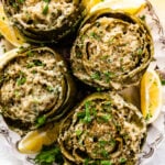 Cooked artichokes on a platter with lemon wedges on the side. Parsley on top.