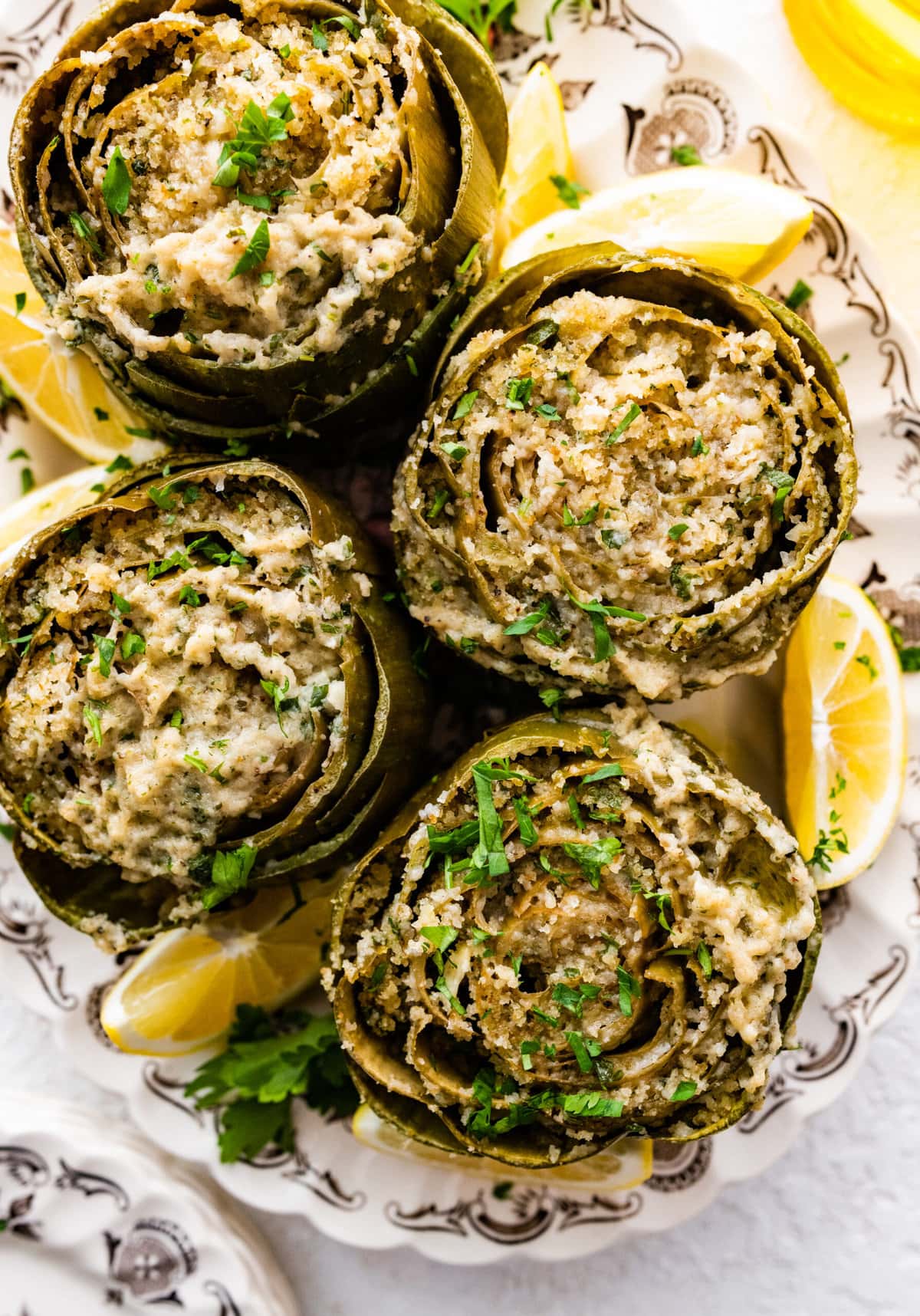 Cooked artichokes on a platter with lemon wedges on the side. Parsley on top.