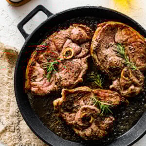 Three lamb shoulder chops cooking in a skillet.