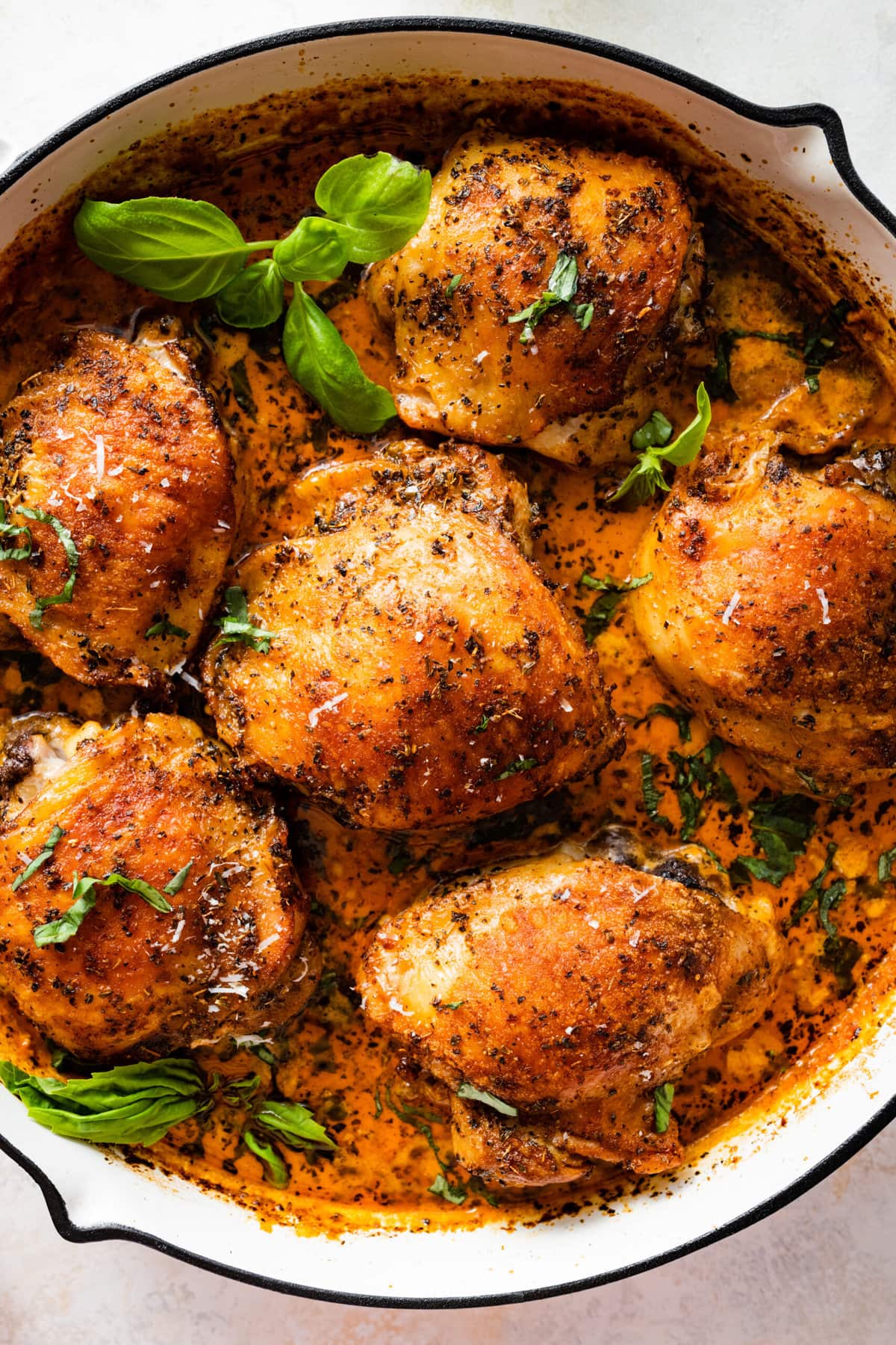 saucy chicken thighs in a pan with sauce. Basil leaves as garnish. 