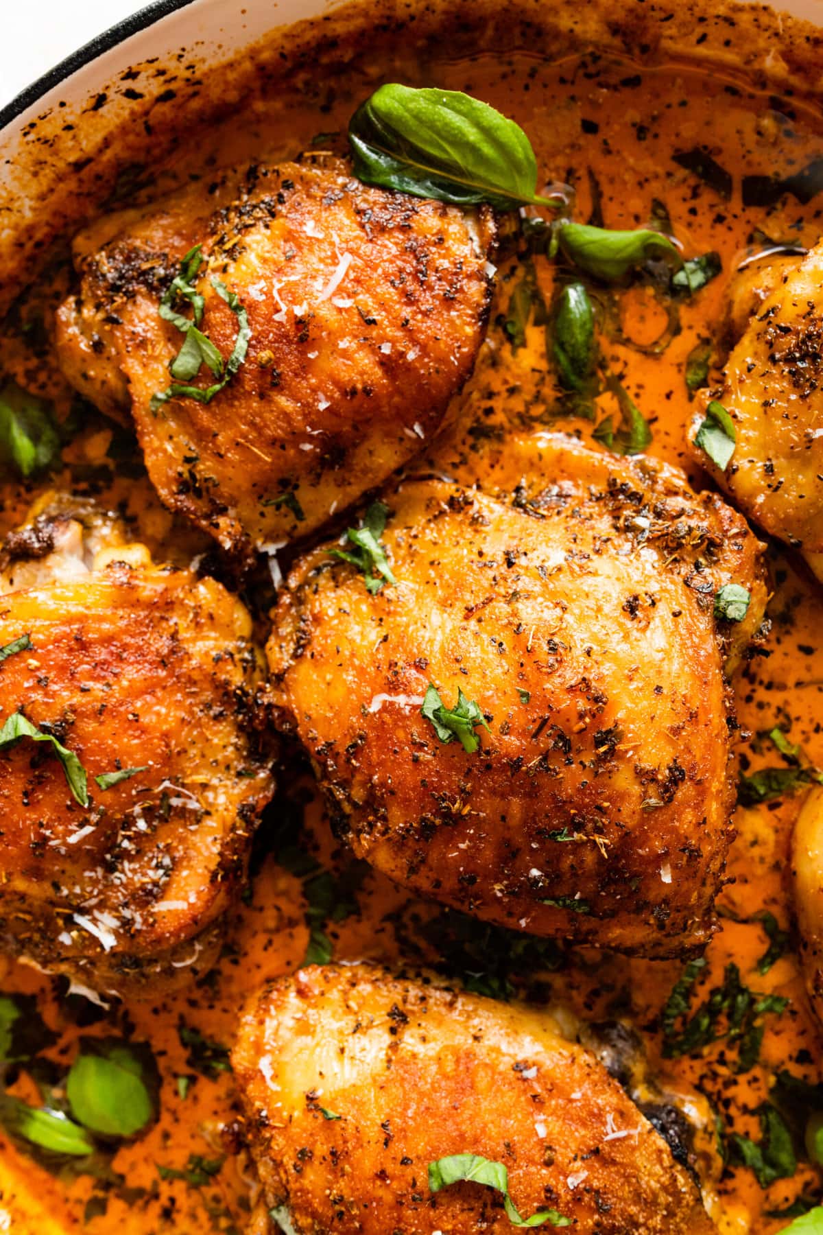 saucy chicken thighs in a pan with sauce. Basil leaves as garnish.