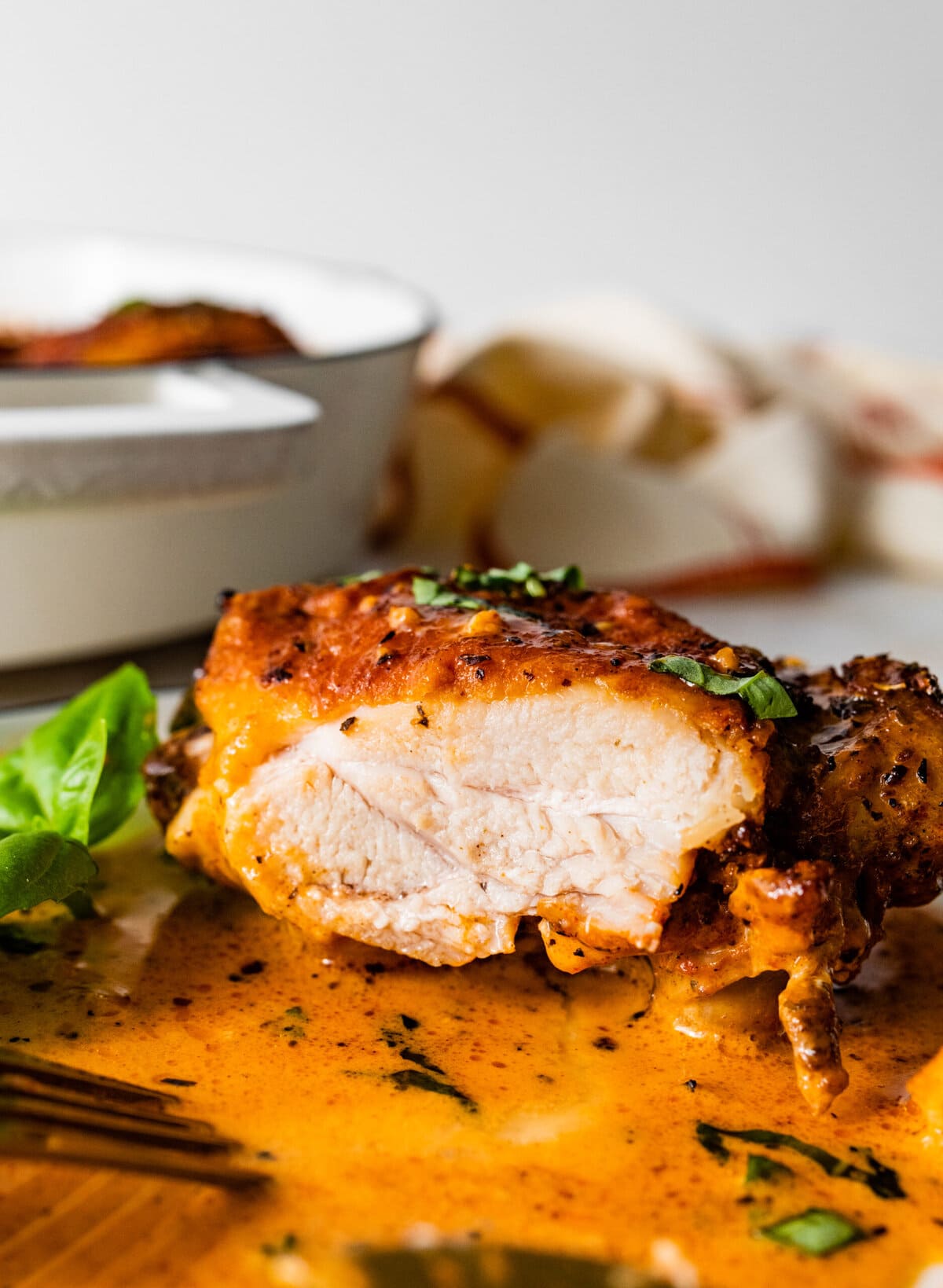 up close of juicy chicken on plate with the pan sauce and a basil leaf.