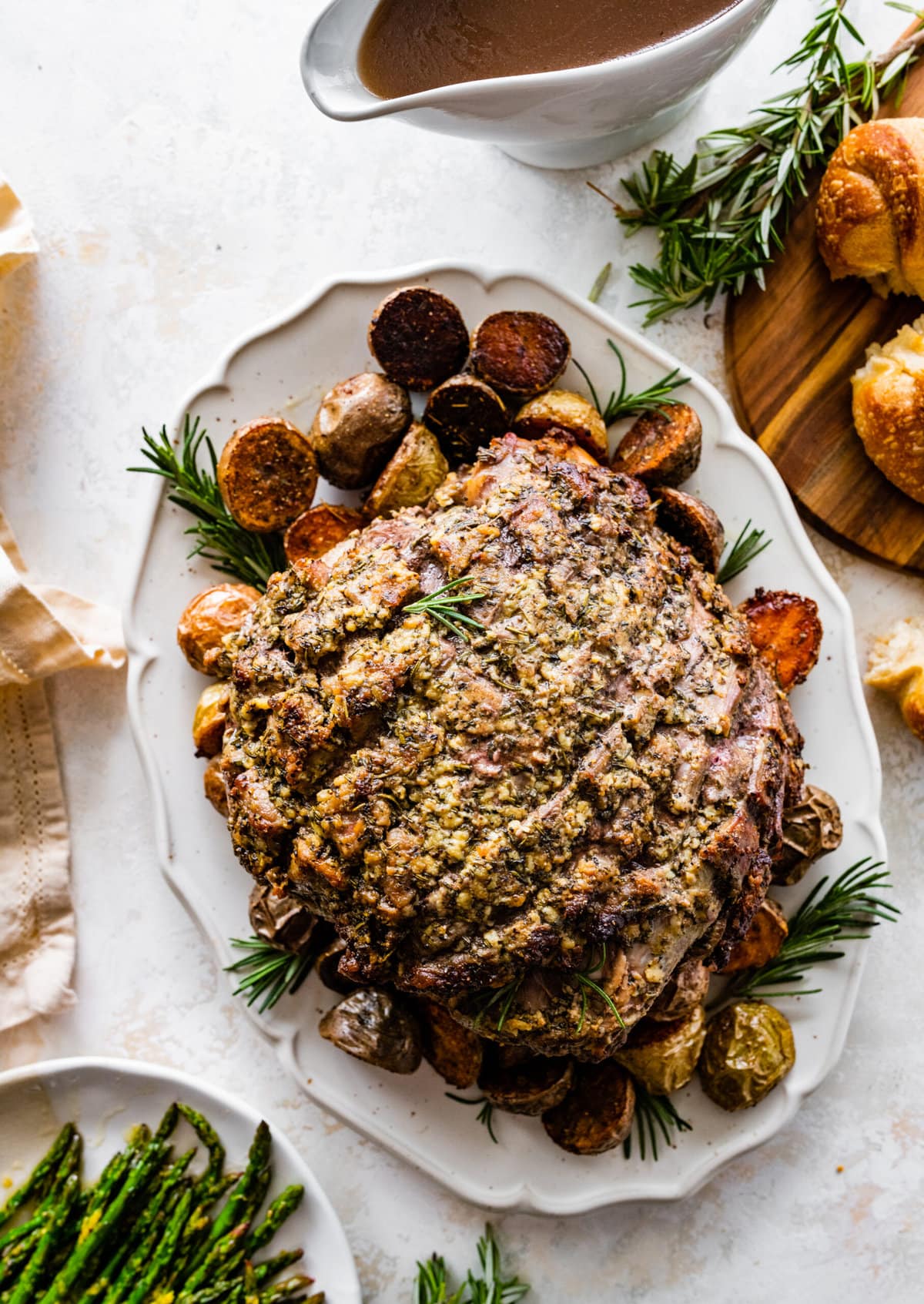 Beautiful lamb roast on a serving platter with potatoes and herbs. 