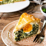 torta pasqualina savory Italian Easter one slice on a plate with a fork. The cooke egg is visible and the spinach filling surrounds it.