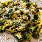 Tuscan roasted broccoli on a serving platter with parmigiano cheese and lemon wedges. Adding toasted pine nuts.