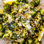 Tuscan roasted broccoli on a platter with parmigiano cheese and lemon topped with toasted pine nuts.