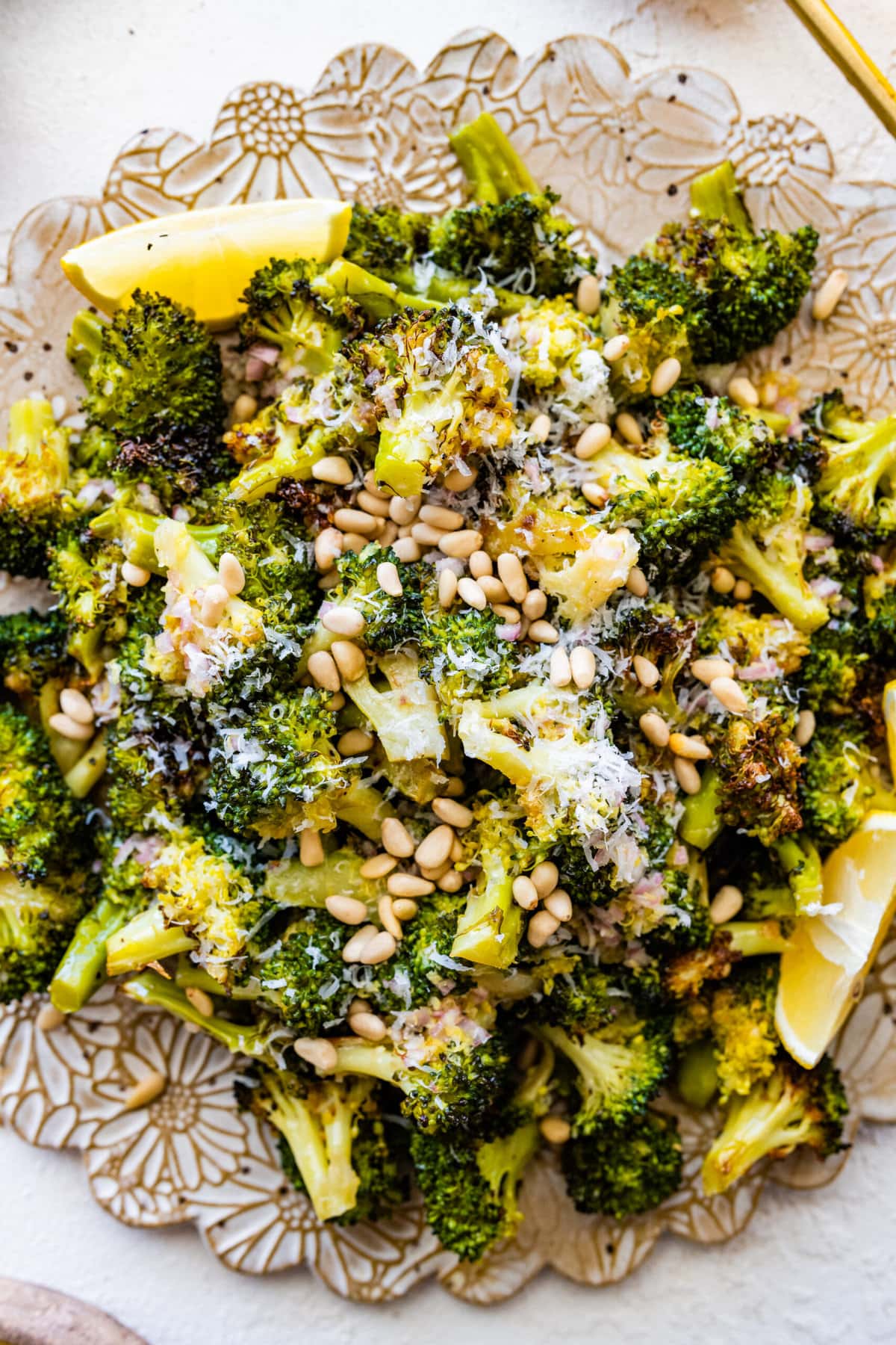 Tuscan roasted broccoli on a serving platter with parmigiano cheese and lemon wedges. Adding toasted pine nuts.