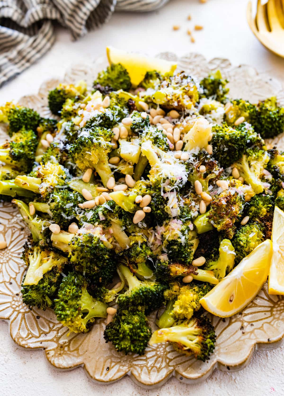 Tuscan roasted broccoli on a serving platter with parmigiano cheese and lemon wedges. Adding toasted pine nuts.