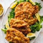 crispy fried pork chops on a plate with salad and lemon wedges.