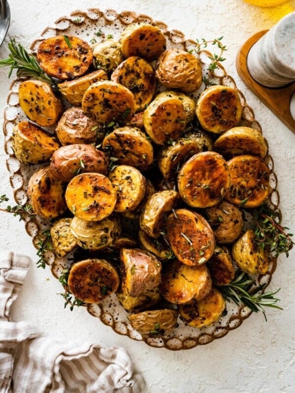 crispy potatoes on a serving platter with fresh herbs around it.
