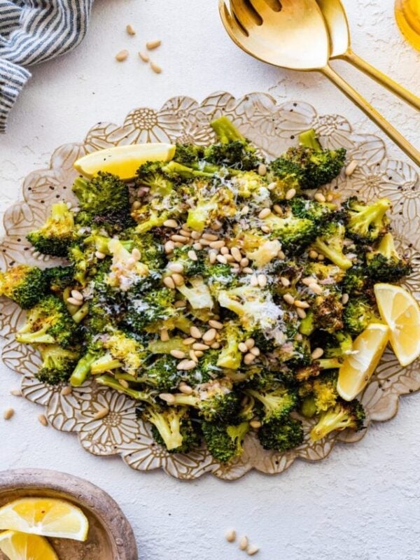 Tuscan roasted broccoli on a serving platter with parmigiano cheese and lemon wedges. Adding toasted pine nuts.