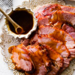 slices of baked ham on a serving platter with brown sugar glaze on the side.