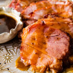 slices of baked ham on a serving platter with brown sugar glaze on the side.
