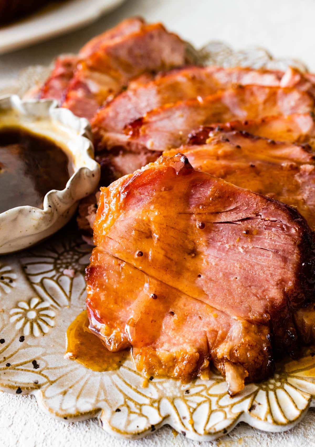 slices of baked ham on a serving platter with brown sugar glaze on the side.