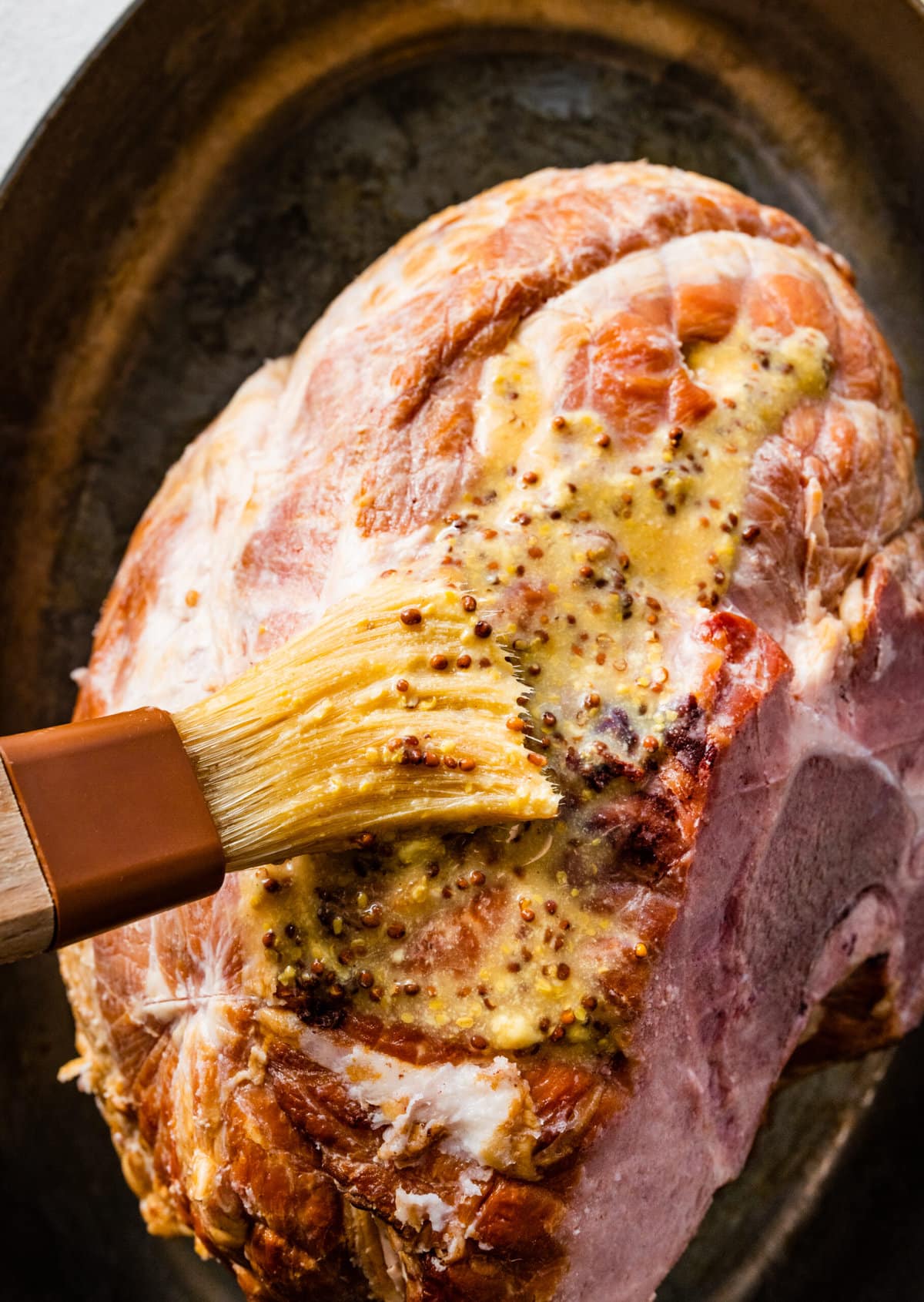 How to make baked ham with brown sugar glaze step-by-step: adding mustard mixture to the ham.
