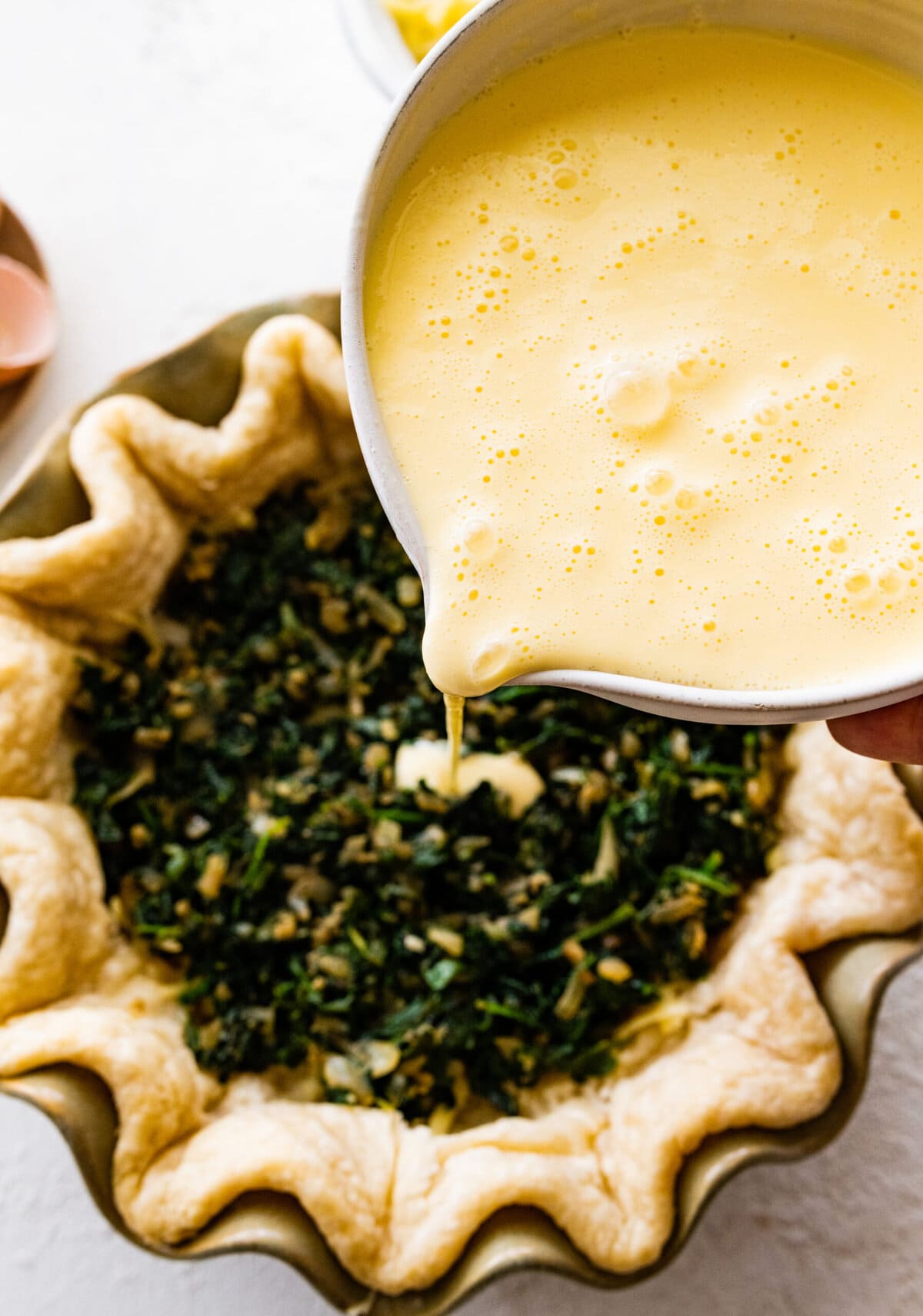 How to make spinach quiche step-by-step: pour egg custard on top of spinach in pie dish.