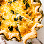 baked spinach quiche recipe out of the oven with golden brown top. Slice taken out with a pie server.