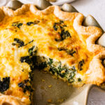 baked spinach quiche recipe out of the oven with golden brown top. Slice taken out.