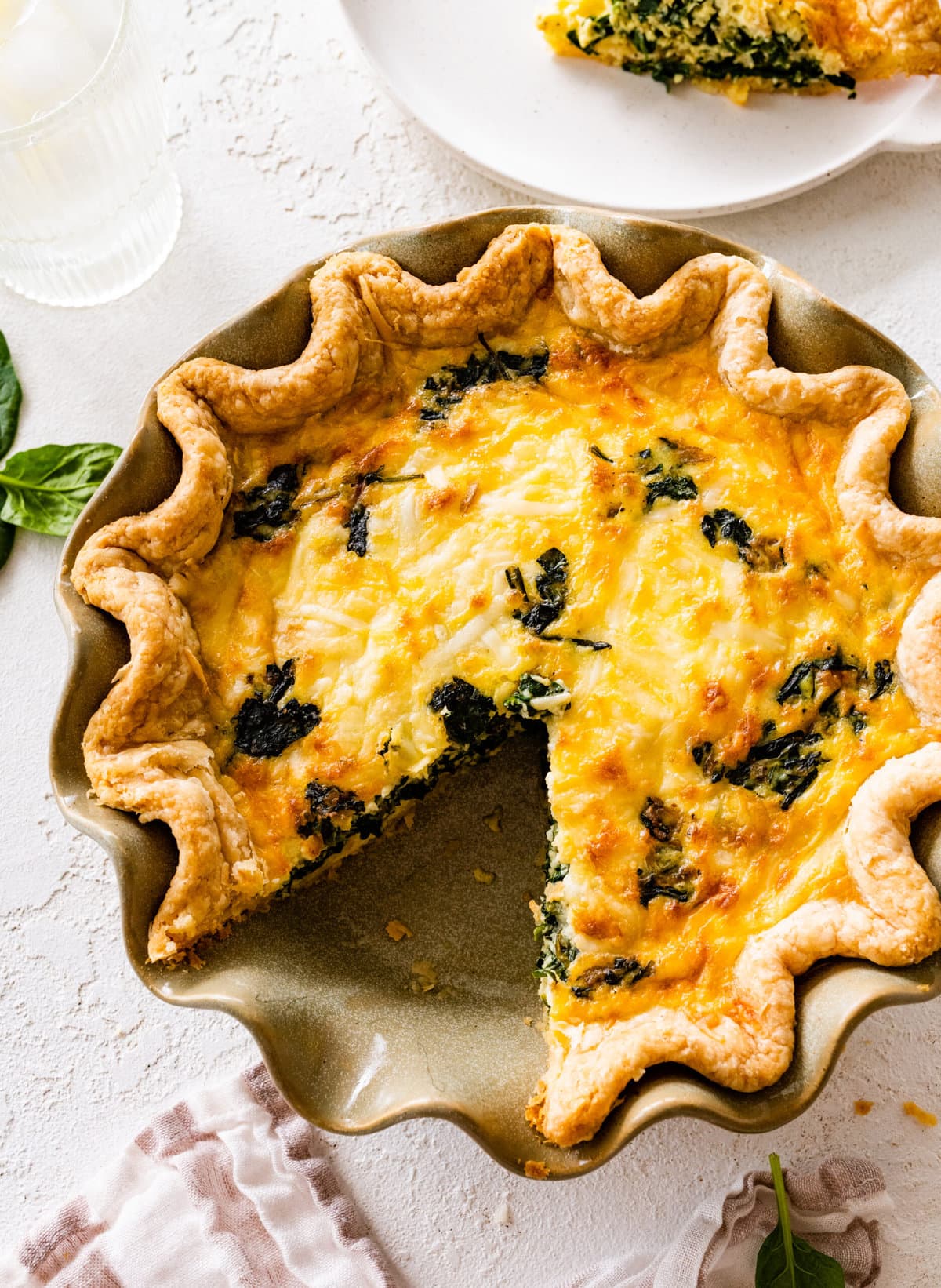 baked spinach quiche recipe out of the oven with golden brown top. Slice taken out.