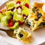 spinach quiche slice on a plate ready to eat. Fork taking a bite.