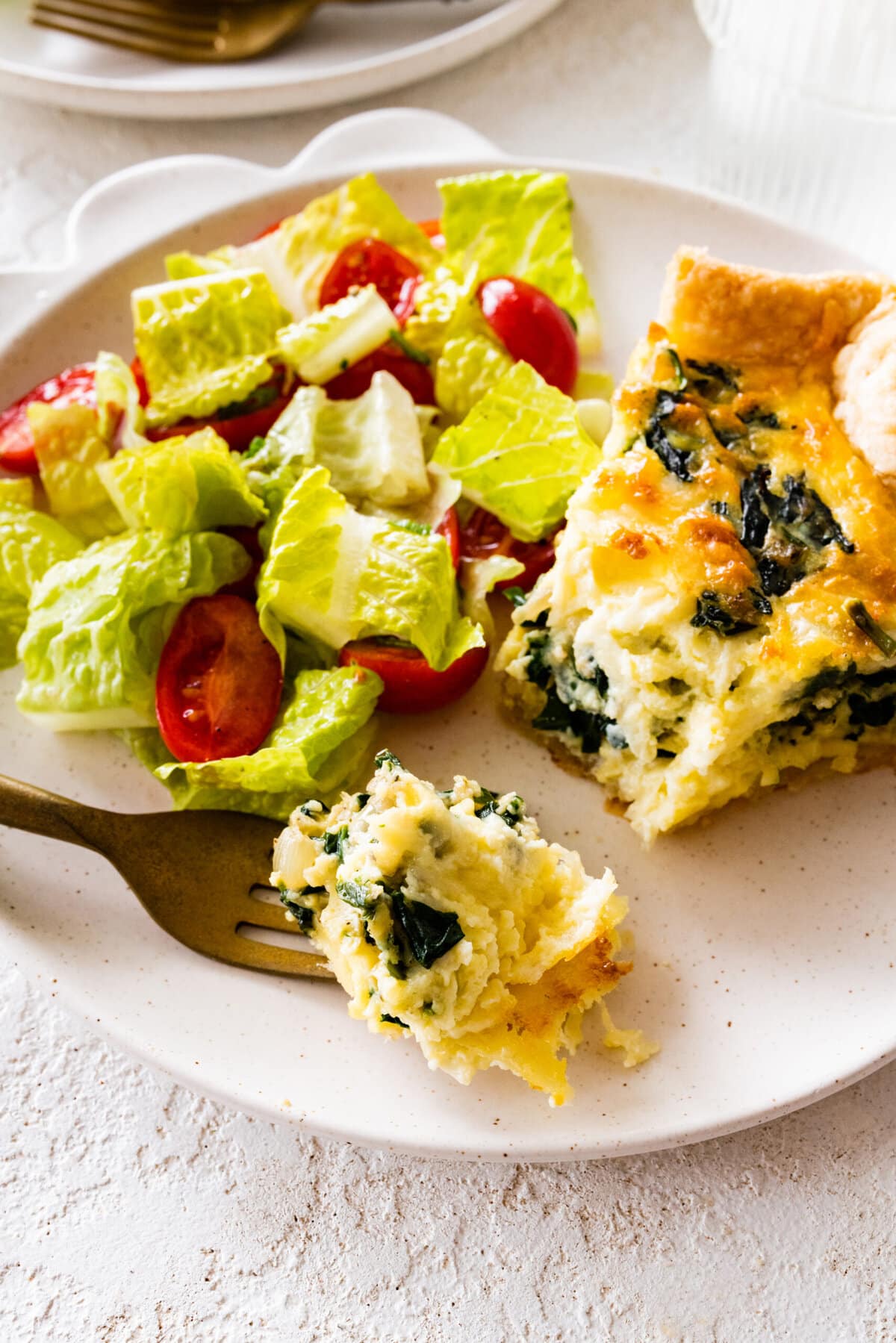 spinach quiche slice on a plate ready to eat. Fork taking a bite.