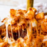 baked cheesy classic pasta al forno recipe out of the oven in a white baking pan. Serving spoon lifting up the pasta al forno with a cheese pull.