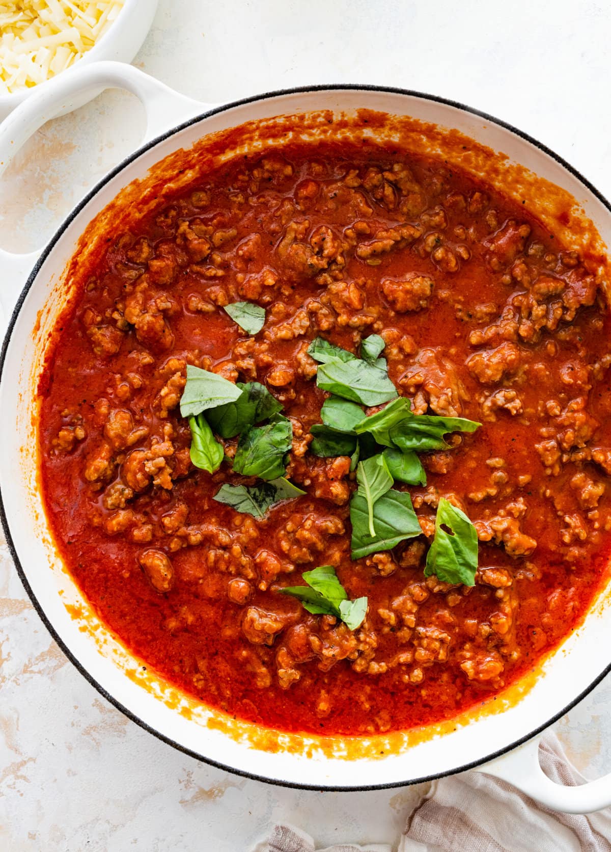 How to make classic pasta al forno step-by-step: adding basil to the pan with meat and sauce.